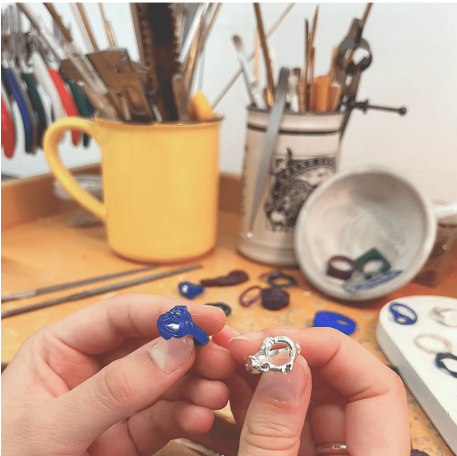 Person holding two small jewelry pieces with a workshop background