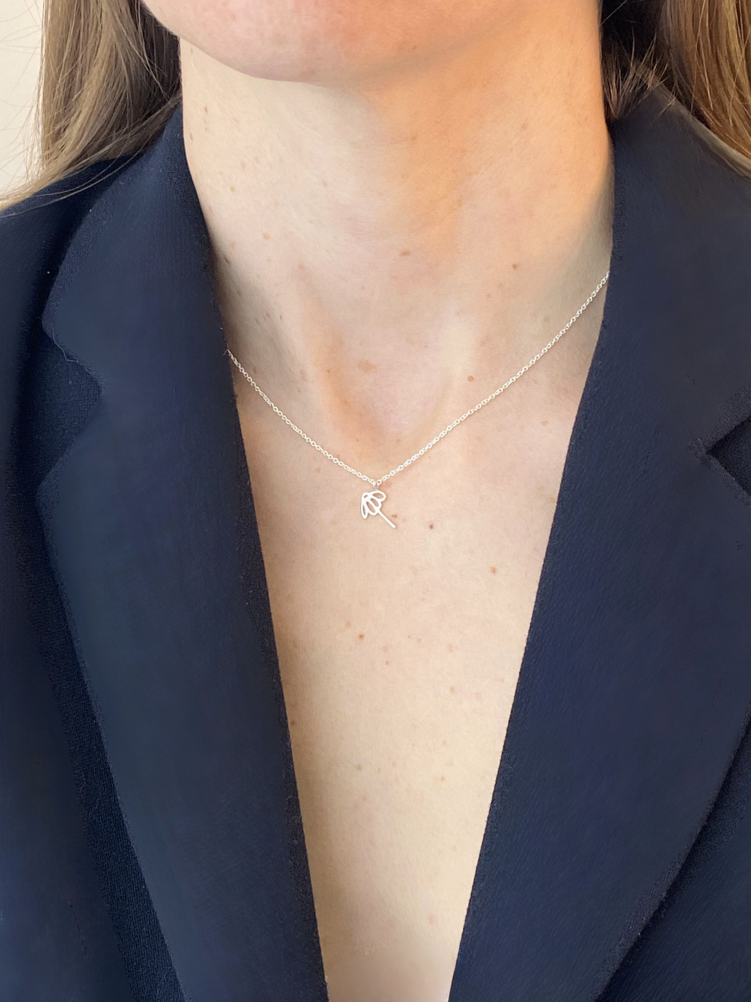 Person wearing a delicate necklace with a small pendant against a dark blue background