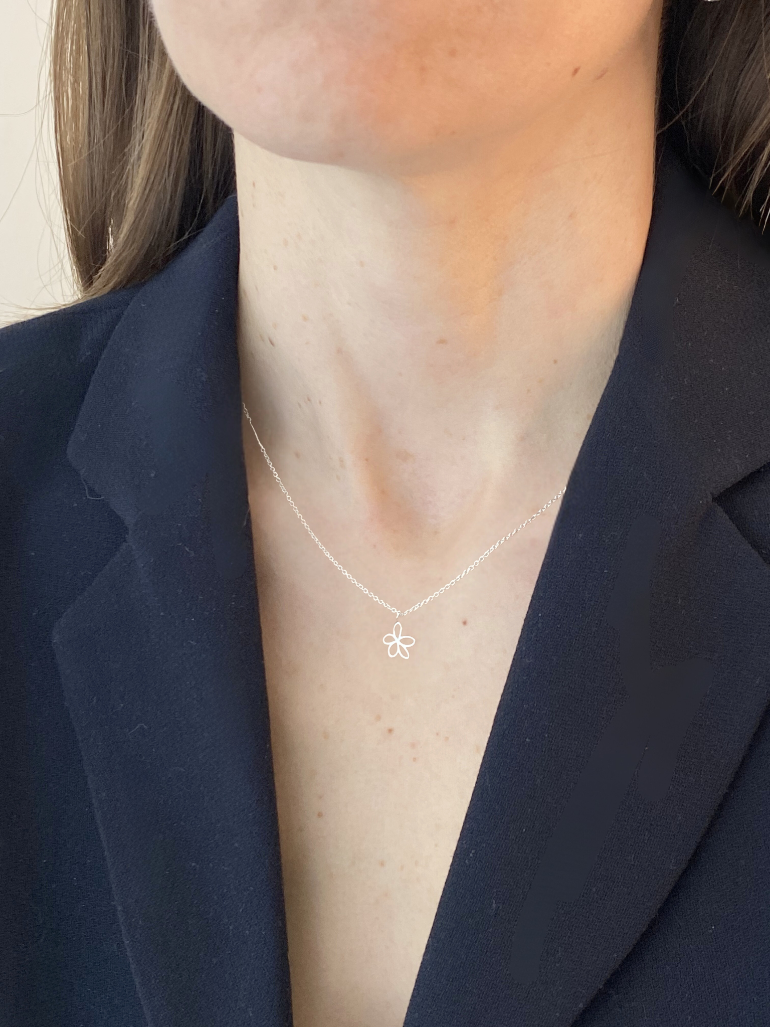 Person wearing a delicate necklace with a small pendant against a neutral background