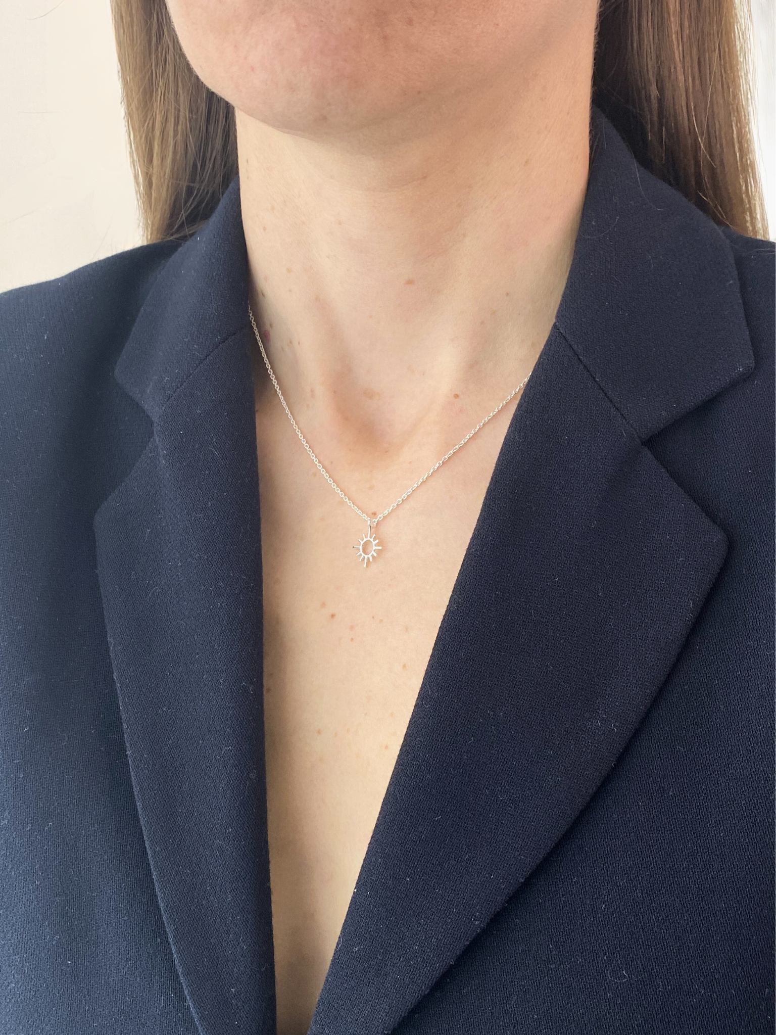 Person wearing a sun necklace with a navy blazer