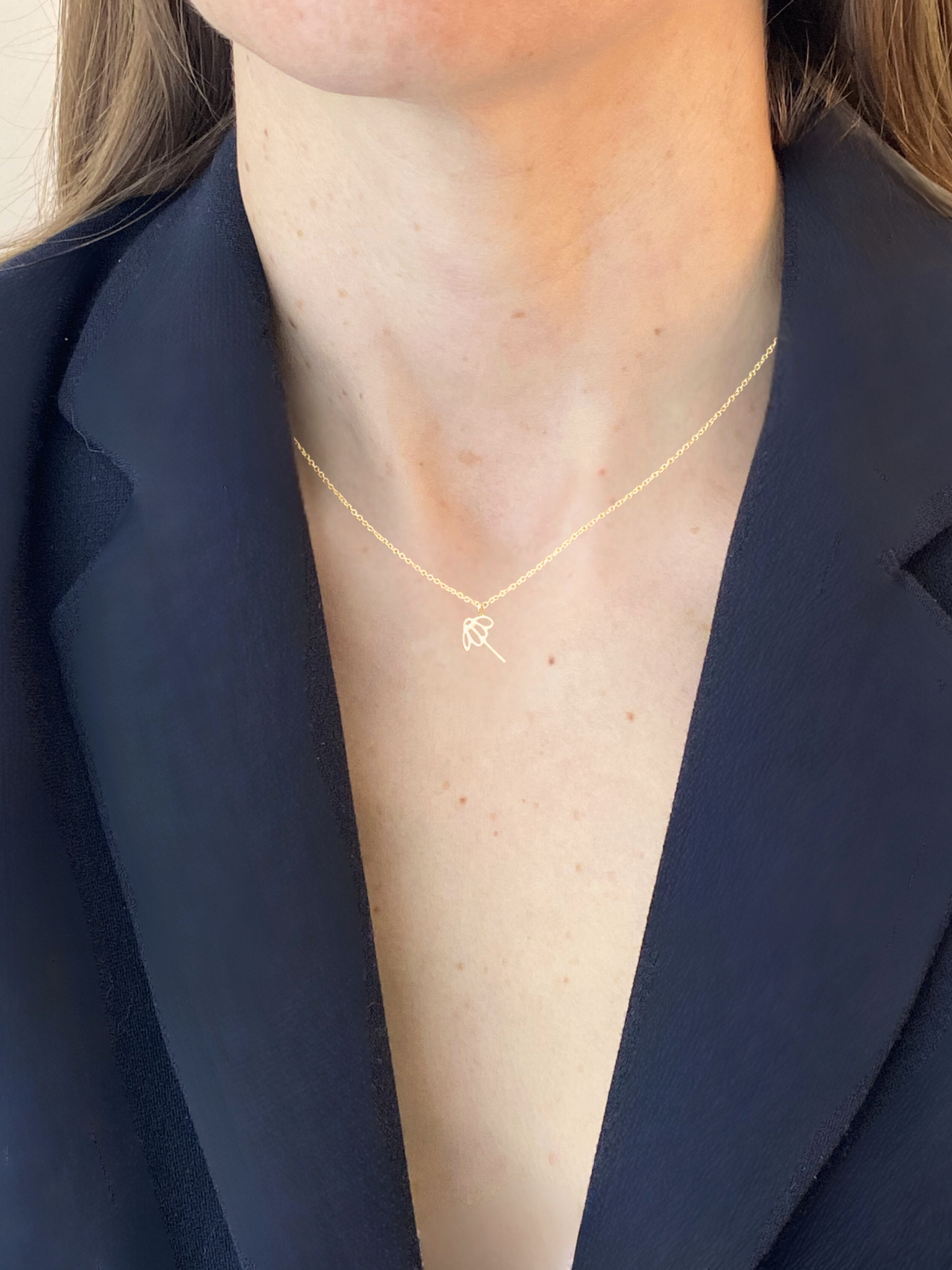 Gold necklace with a sunflower pendant worn by a person in a navy blazer.